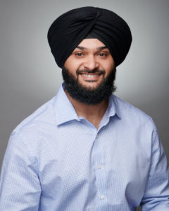 Professional headshot of a smiling man wearing a light blue dress shirt and black turban.