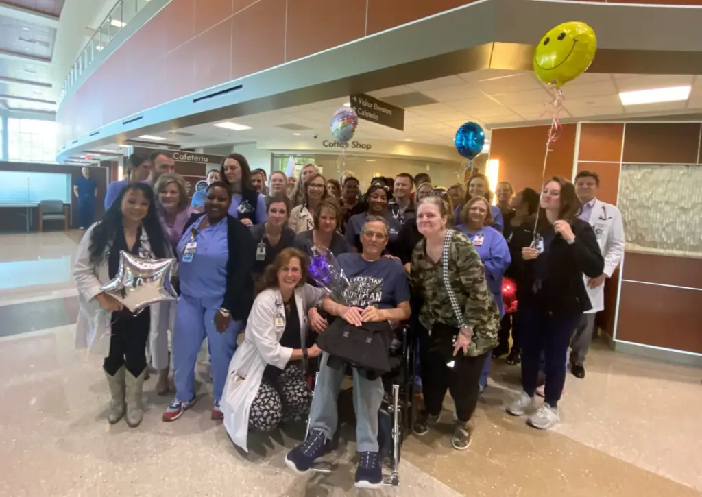 Group of people accompanying a man in a wheelchair inside a hospital