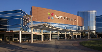 A modern hospital exterior with large glass windows reflects the sky. 