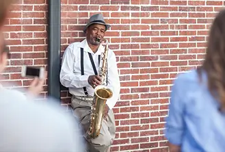 man leaning on a street brick wall playing saxophone