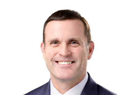 Evan Howell, smiling in a dark suit and white shirt against a plain white background. His expression conveys friendliness and professionalism.