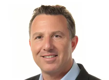 Headshot of Andrew Kassinove, smiling, wearing a black blazer and a blue button-down shirt.