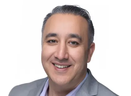 Headshot of Tariq Noohani, smiling, wearing a grey blazer and a lavender button-down shirt.