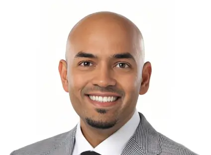 Headshot of Yogin Patel smiling, wearing a bgrey plaid and a white button-down shirt.