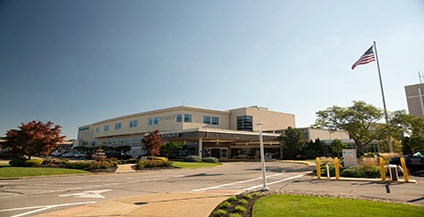 Exterior of MercyOne Centerville Medical Center at night, with illuminated signage. An American flag waves above the brick building against a dark sky.