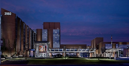 Nighttime view of a modern hospital building with large glass windows and a central entrance, illuminated under a deep blue sky, conveying a calm ambiance.