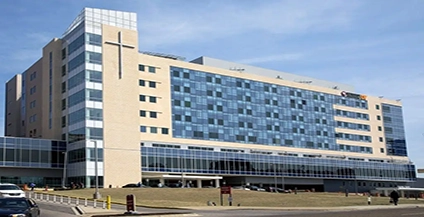 Large modern hospital with glass facade and cross symbol, under a clear blue sky. Building conveys a sense of professionalism and care.