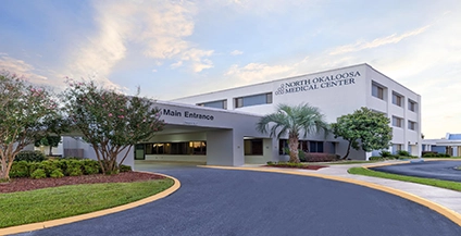 The image shows the exterior of North Okaloosa Medical Center, a modern white three-story building with 