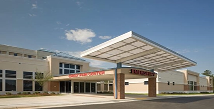 Modern hospital entrance with a covered driveway. Signage for emergency services is visible. Clear blue sky adds a welcoming tone.