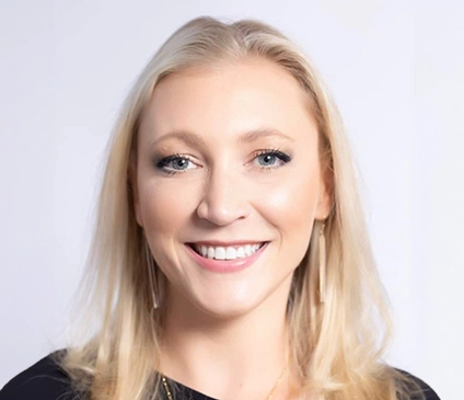 A professional headshot of Sara Gunter, a woman with blonde hair wearing a dark suit jacket and a white blouse, set against a neutral, light-colored background.