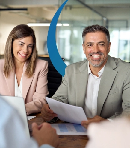 Smiling man and woman in business attire sit at a conference table holding papers, conveying a professional and collaborative atmosphere.