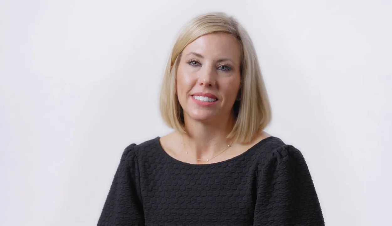 Smiling female doctor with curly hair uses a tablet in a bright medical office. Two blurred colleagues in the background, creating a professional atmosphere.