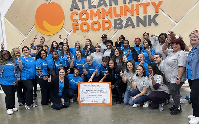 A group of volunteers in blue 'ApolloMD' shirts working together at the Atlanta Community Food Bank to sort and pack food for those in need.