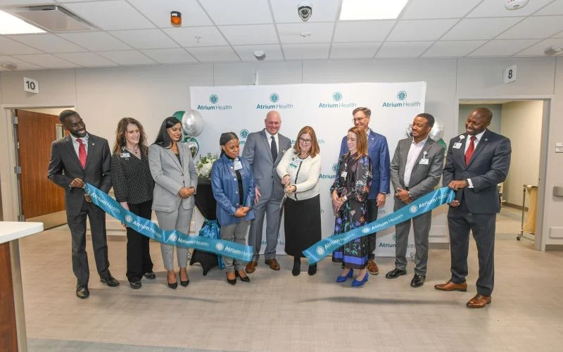 Professional group in front of the Atrium Health logo displayed in teal and blue text against a clean white background, representing a collaborative healthcare announcement.
