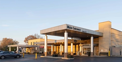 Alt text: Modern hospital entrance with large metal awning, glass doors, and clear signage reading 