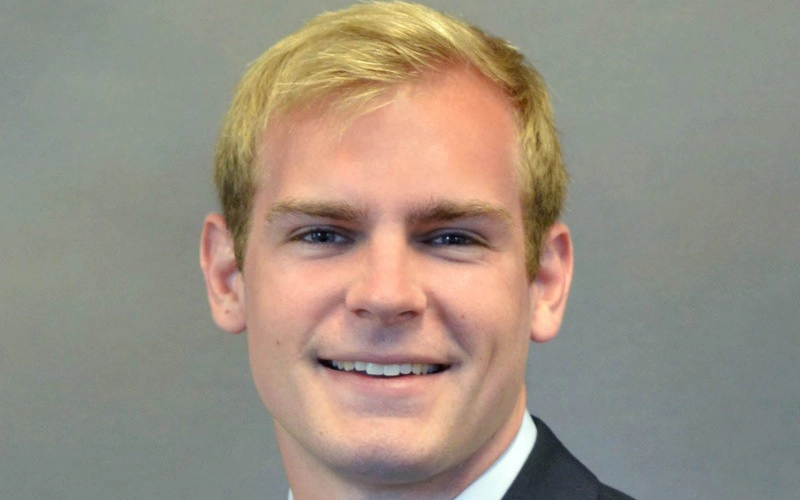 Professional headshot of Andrew Smith, wearing a dark suit jacket and a blue patterned tie against a neutral background.