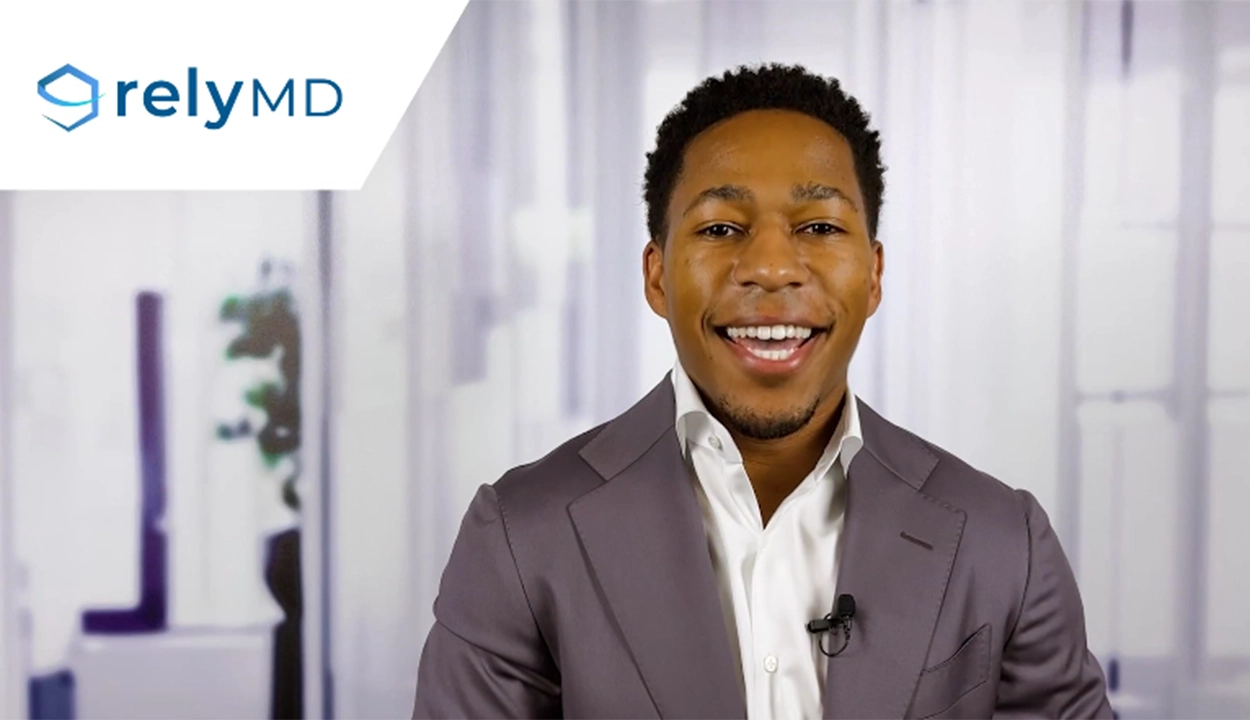 A video still of Dany Accilien, a man speaking in a professional setting with a blurred background