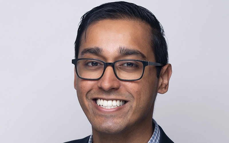 Professional headshot of Saket Kumar, a man wearing a white medical lab coat over a blue button-down shirt and a patterned red and blue tie.
