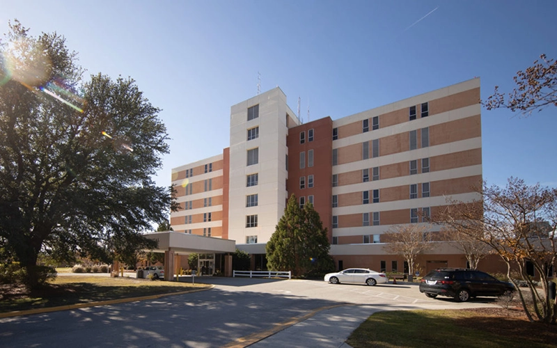 A wide exterior shot of the Onslow Memorial Hospital building, showing the multi-story medical facility with glass and concrete architecture under a clear sky.