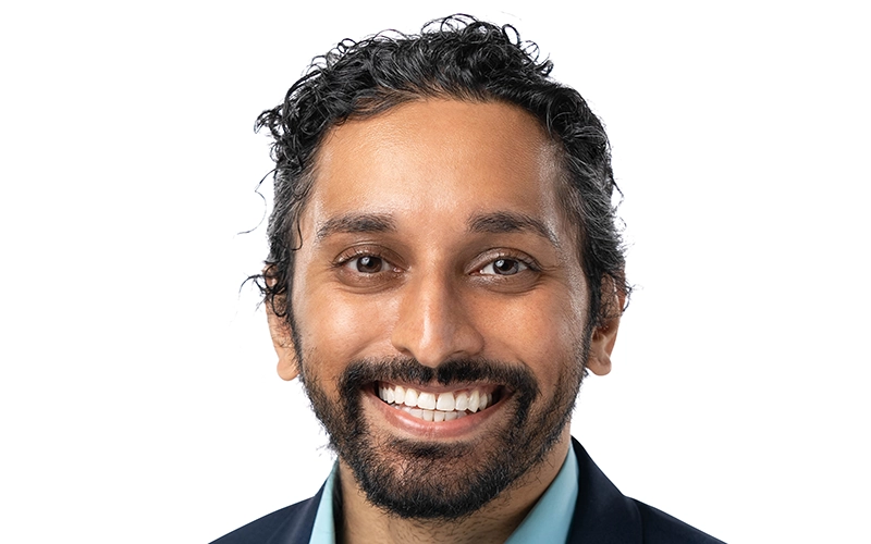 Professional headshot of Dr. Mayur Patel, a man wearing a white medical lab coat over a light blue shirt and dark tie, set against a solid gray background.