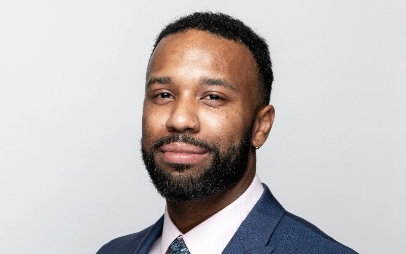 Professional headshot of Rico Beuford, wearing a coat and a blue shirt.
