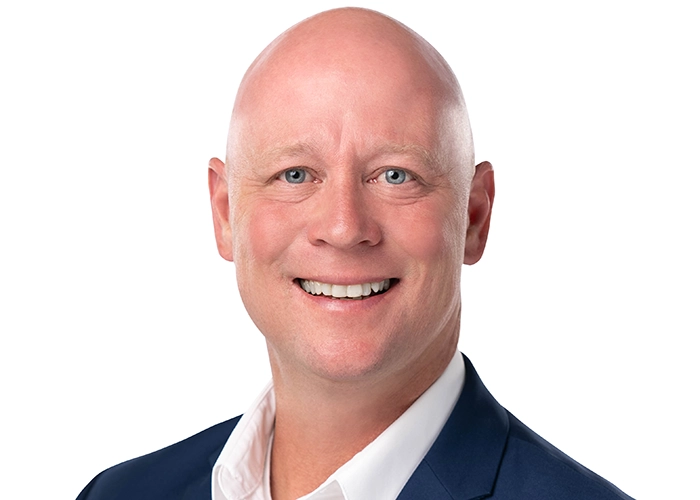 Brent Curry, blue eyes and a warm smile is wearing a dark suit and white shirt against a plain white background. The tone is friendly and professional.