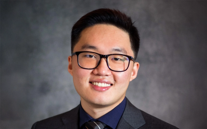 A warm, professional portrait of professional. He has short hair, is wearing a blazer, and is smiling directly at the camera against a neutral backdrop.