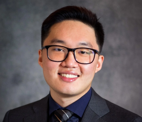 Smiling female doctor with curly hair uses a tablet in a bright medical office. Two blurred colleagues in the background, creating a professional atmosphere.