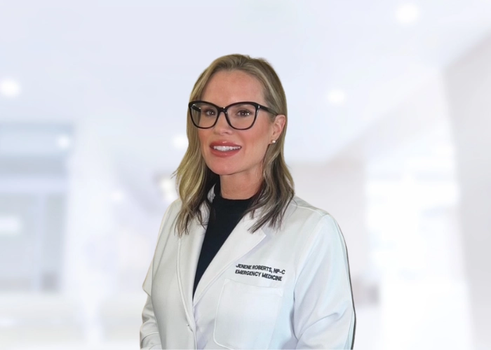 Jenny Roberts, NP-C, Emergency Medicine Nurse Practitioner at ApolloMD, smiling in her white coat in a hospital corridor.