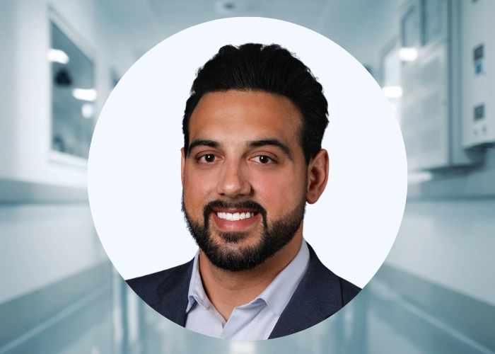 Christian Casteel, DO, smiling in business casual attire, headshot over hospital corridor background.
