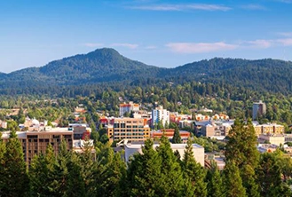 City view with buildings, green trees, mountains, and blue skies of Eugene, Oregon