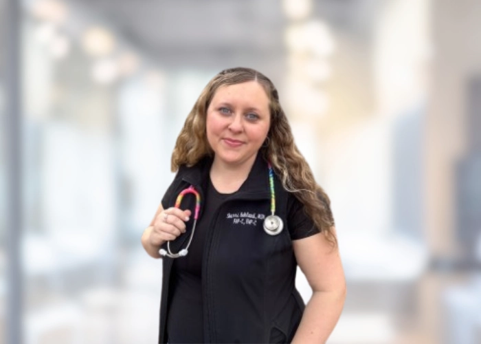 Sherri Bakland, NP-C, in black scrubs with a stethoscope, smiling in a hospital hallway