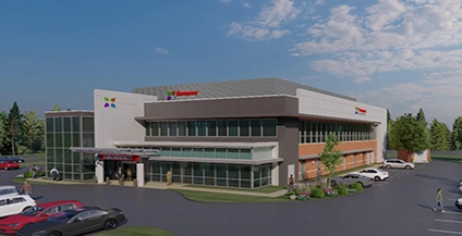 Two-story building with large windows, labeled 'Emergency Urgent Care'. A parking lot and trees are in front under a blue sky.
